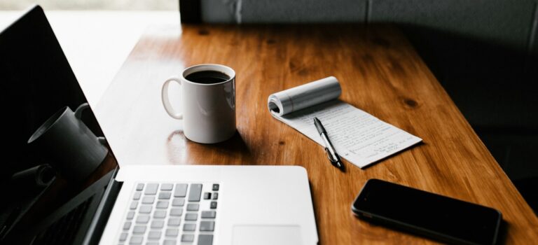 MacBook Pro, white ceramic mug,and black smartphone on table